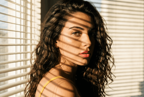 Image générée par IA d'une jeune femme cheveux bouclée devant la fenêtre avec un store